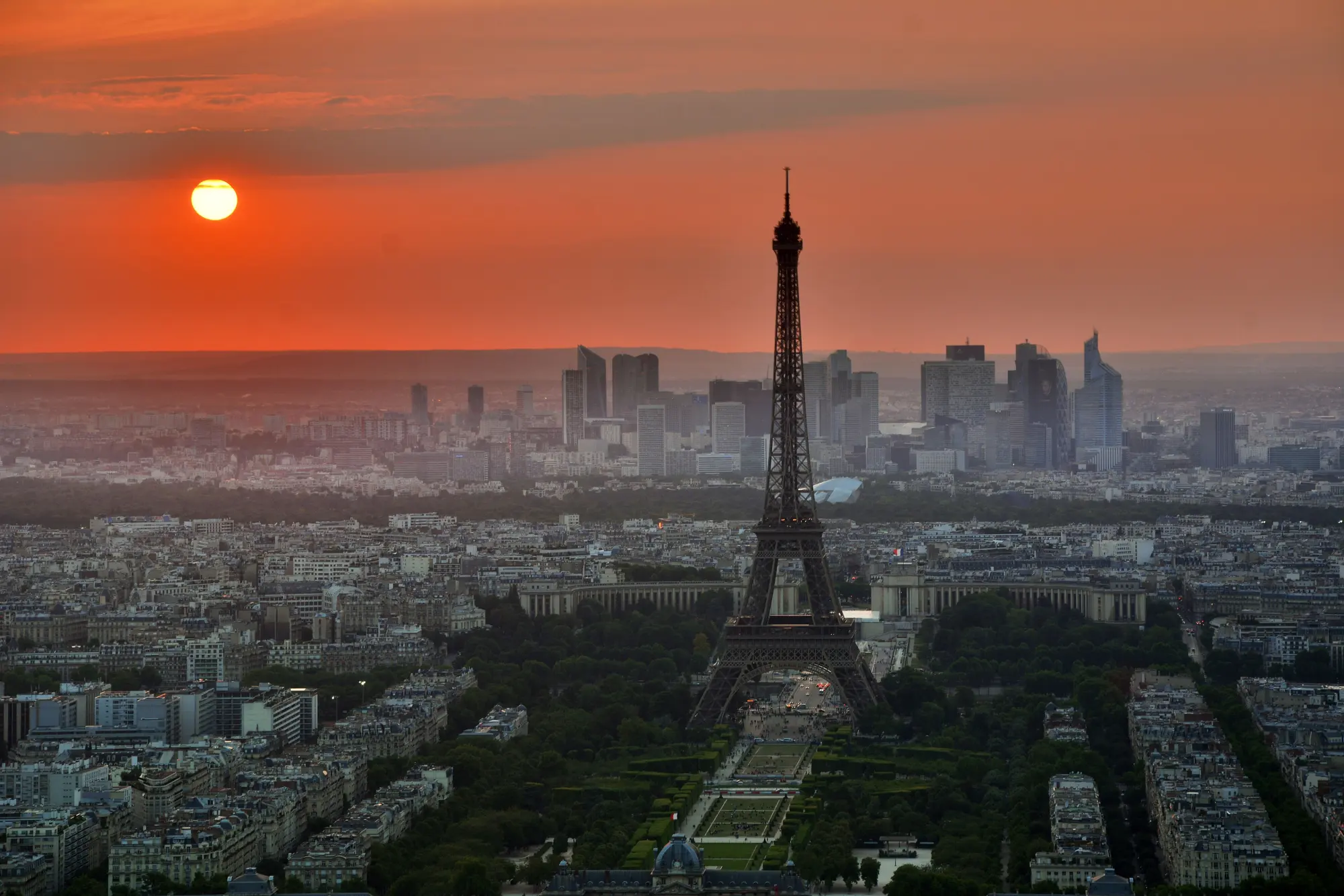 The Eiffel Tower in silhouette at sunset, with the La Défense business district on the horizon behind it